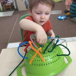 August practising his fine motor skills with the pipe cleaner colander