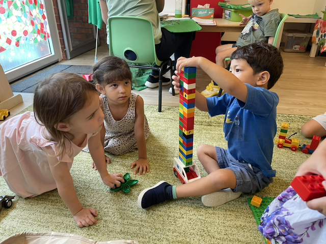 Mia and Alara observing Isaac building a tall tower.