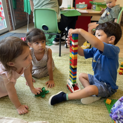 Mia and Alara observing Isaac building a tall tower.