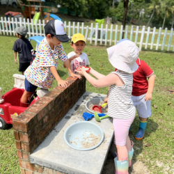 Alex and Luca buying ice cream from the mud kitchen “ ice-cream shop “.