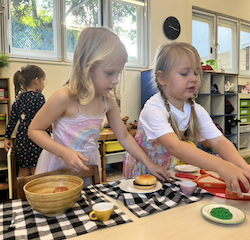 Izzy and Regan laying down their dining table with lots of yummy food .