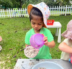 Archish is pouring and scooping in the mud kitchen.